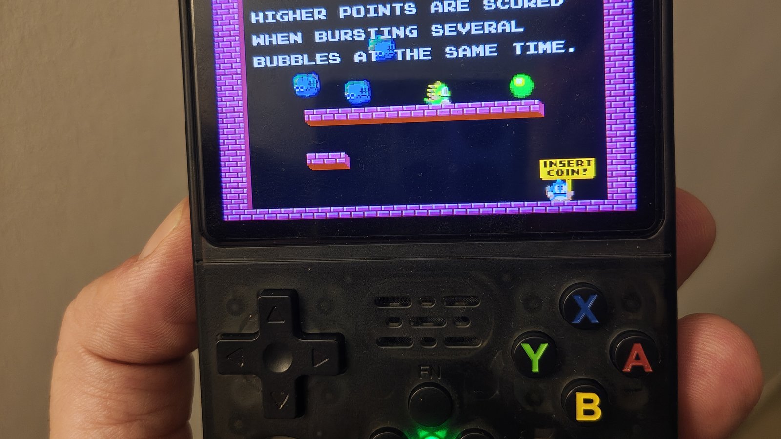 R36S con guscio nero trasparente tenuta in mano con Bubble Bobble sullo schermo